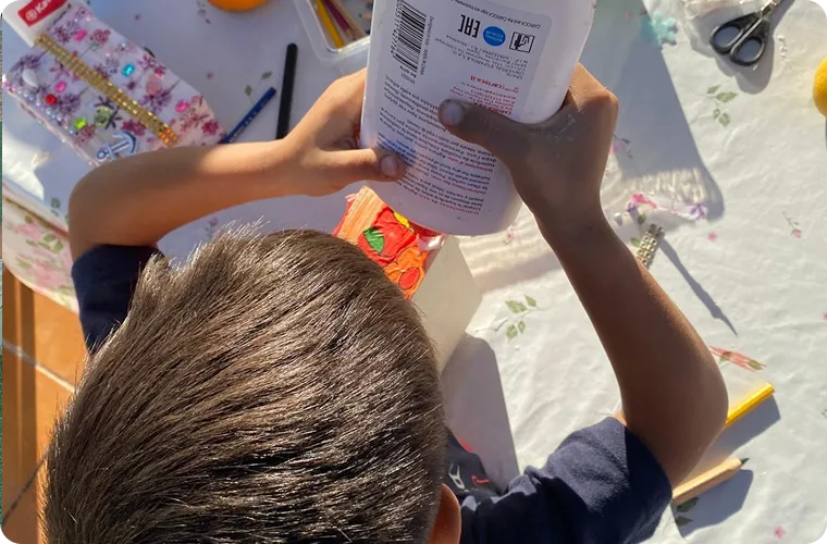 Un niño sostiene un bote de pintura en una mesa de manualidades