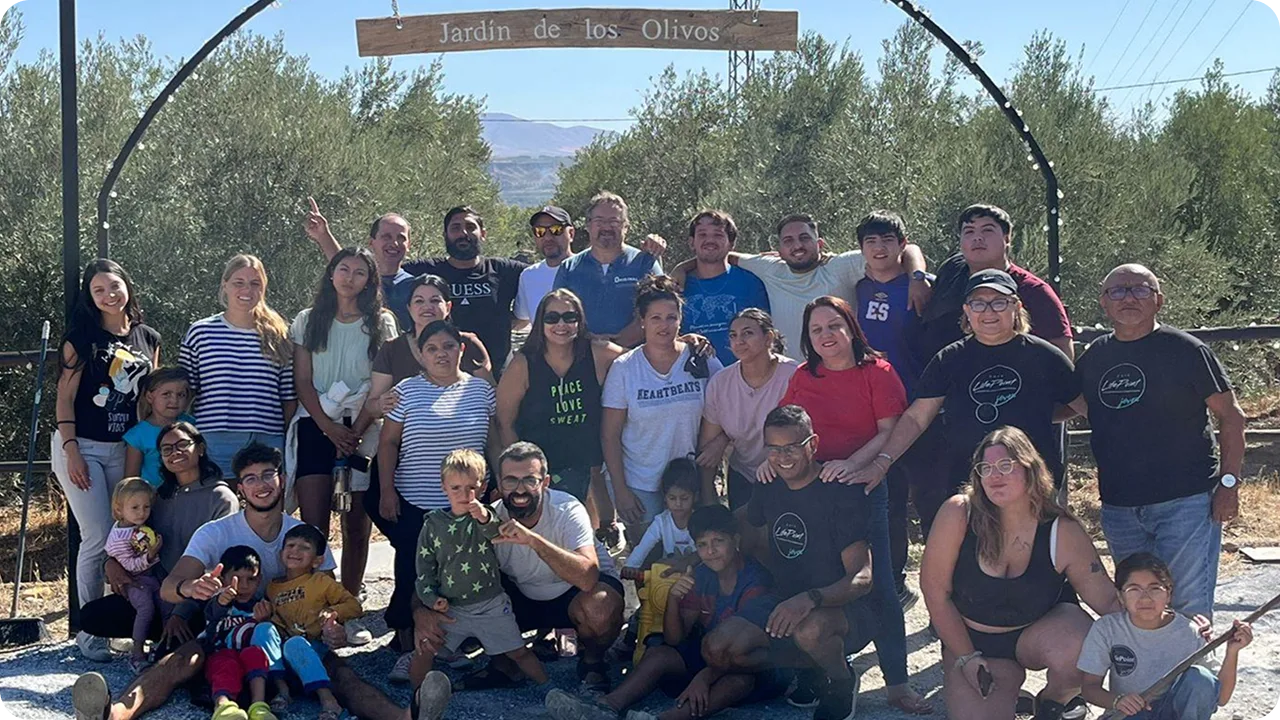 Foto de grupo de la reunión de servidores de 2024, bajo un arco con el rótulo Jardín de los Olivos